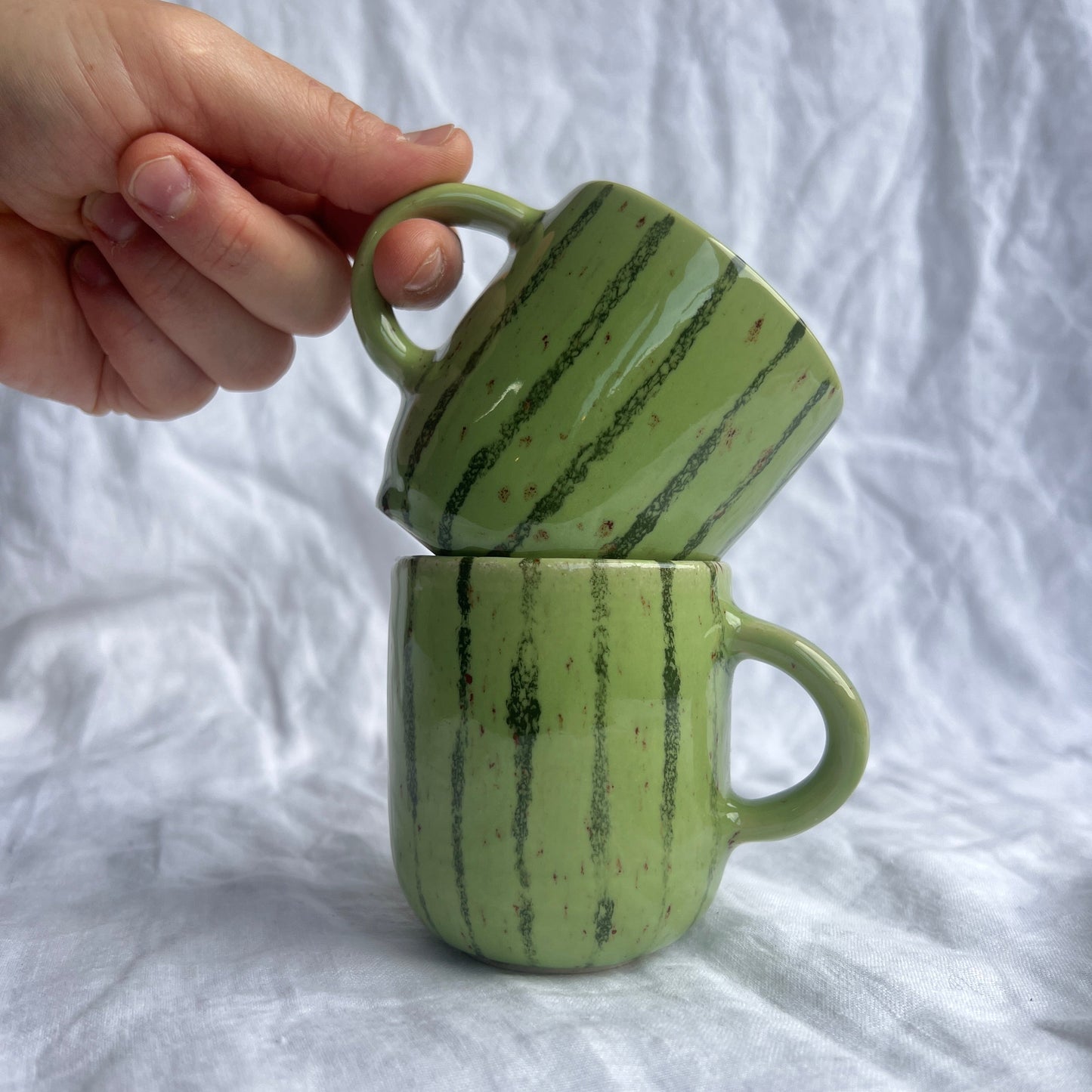 Green ceramic mug with marbled pattern held against a white fabric background