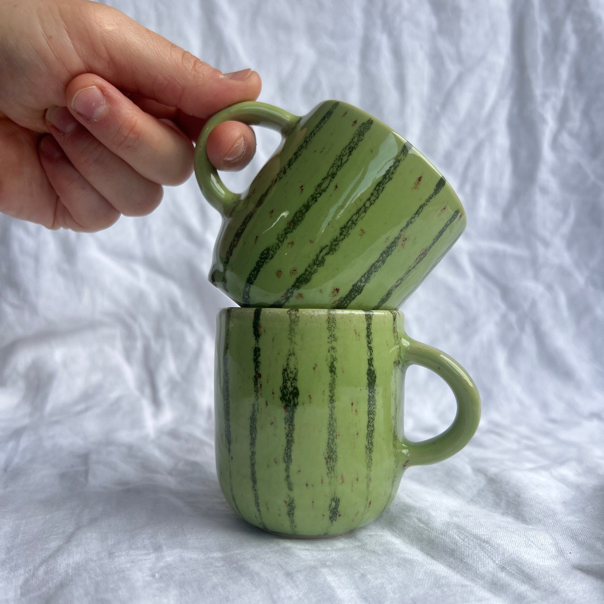 Green ceramic mug with marbled pattern held against a white fabric background