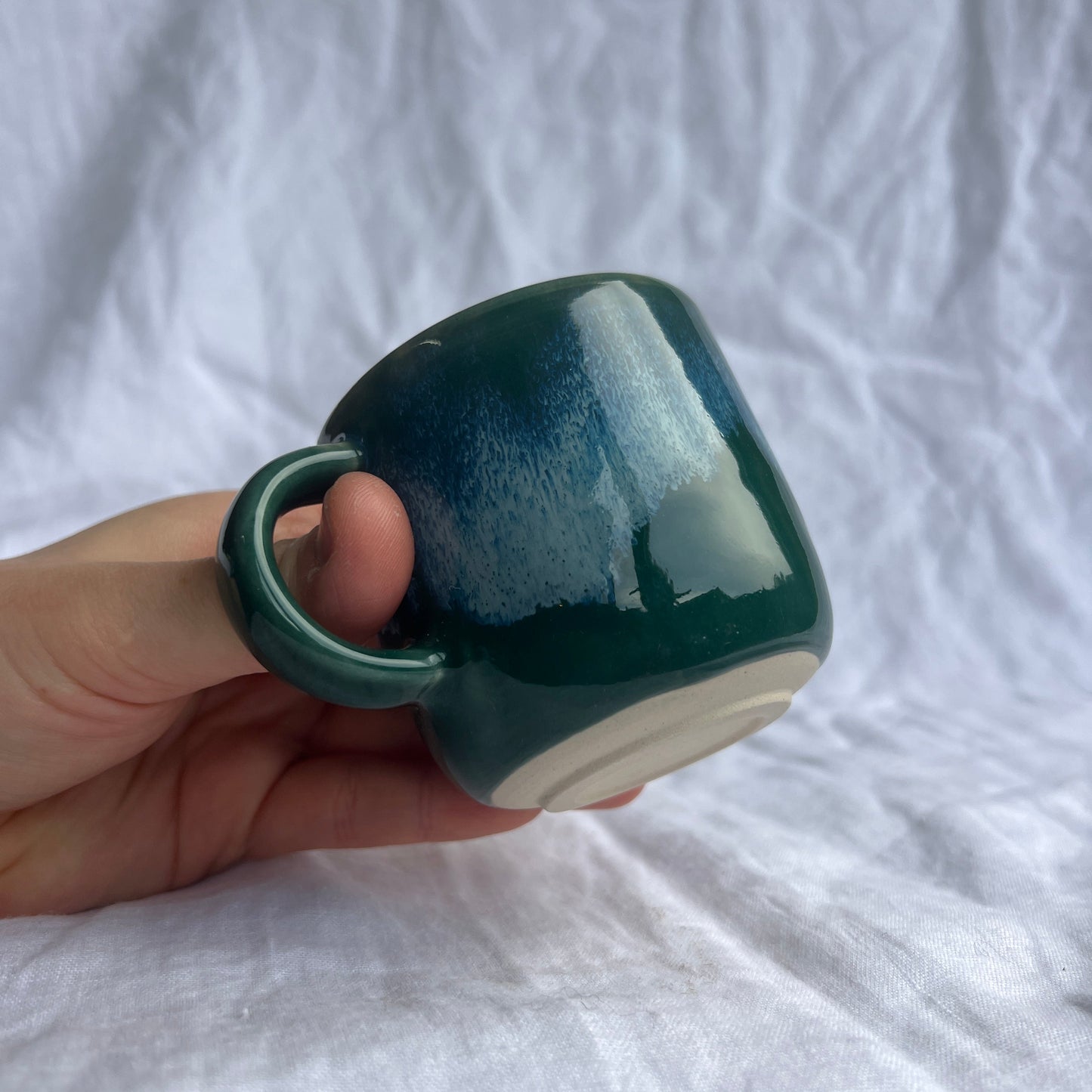 Hand holding a green and white mug against a white background